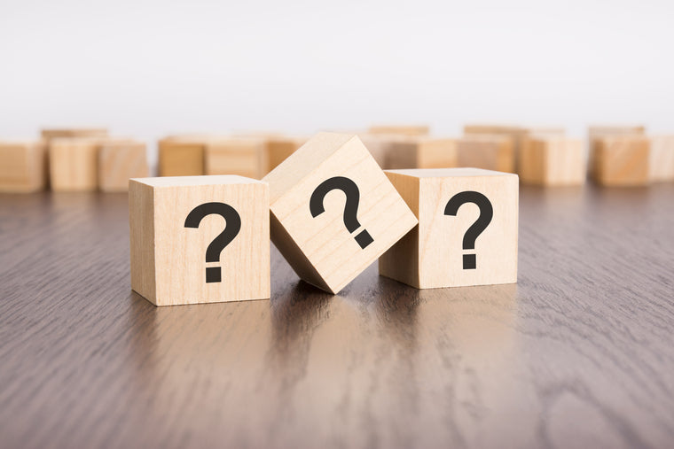 three wooden blocks with question marks in the foreground in a conceptual image on dark
